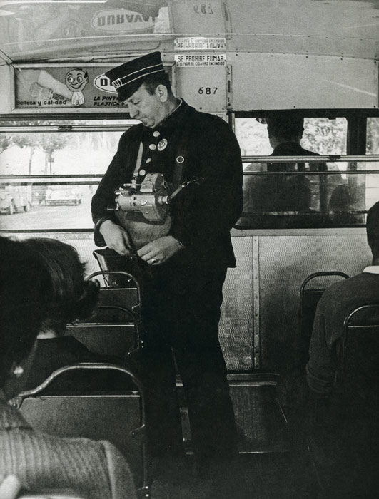 1967. Con r�gida uniformidad, gorra incluida, un cobrador desempe�a su trabajo a bordo de un autob�s (con el volante a la derecha)